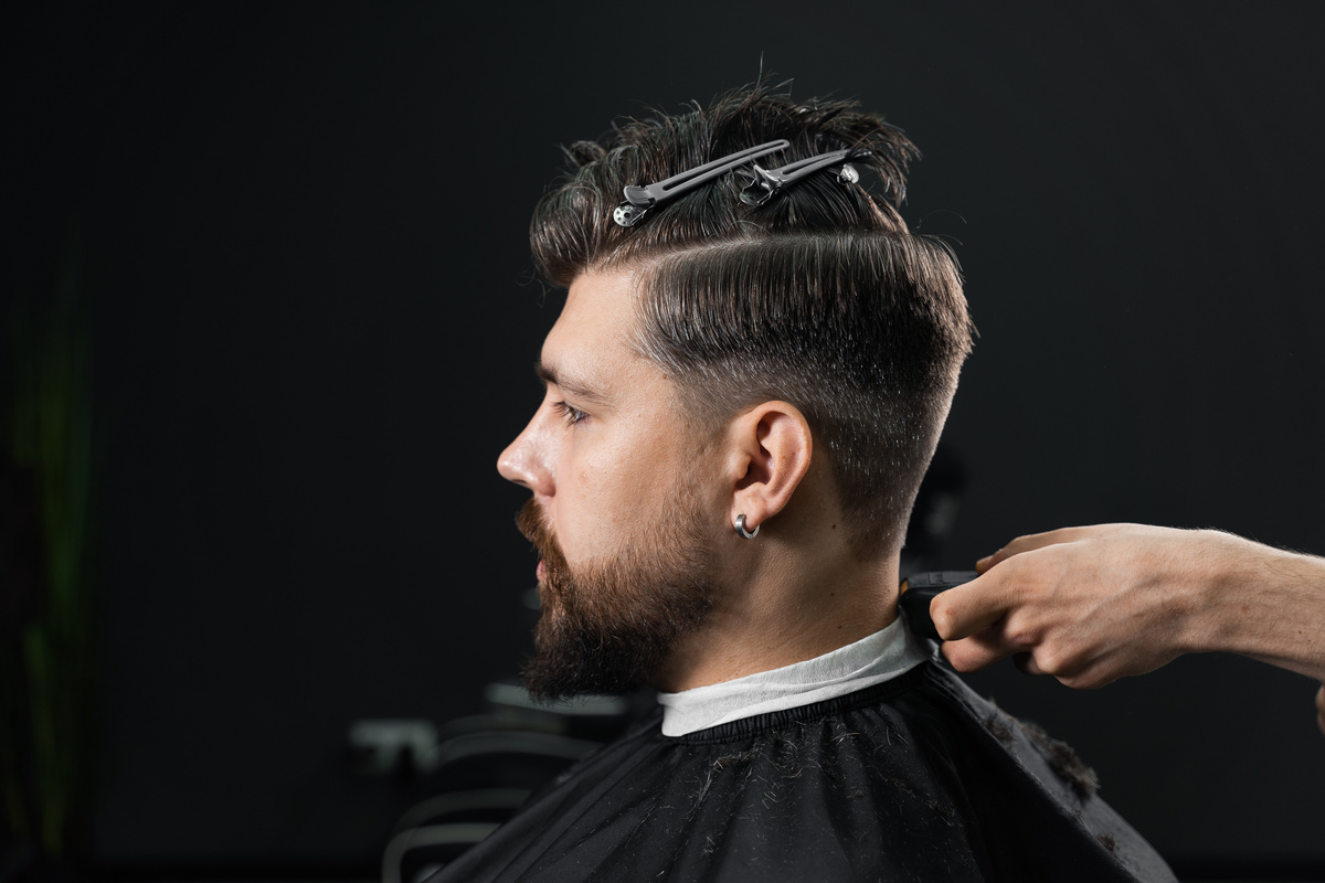 Low fade machine haircut for handsome bearded man in barbershop. Hair cut with a smooth transition.